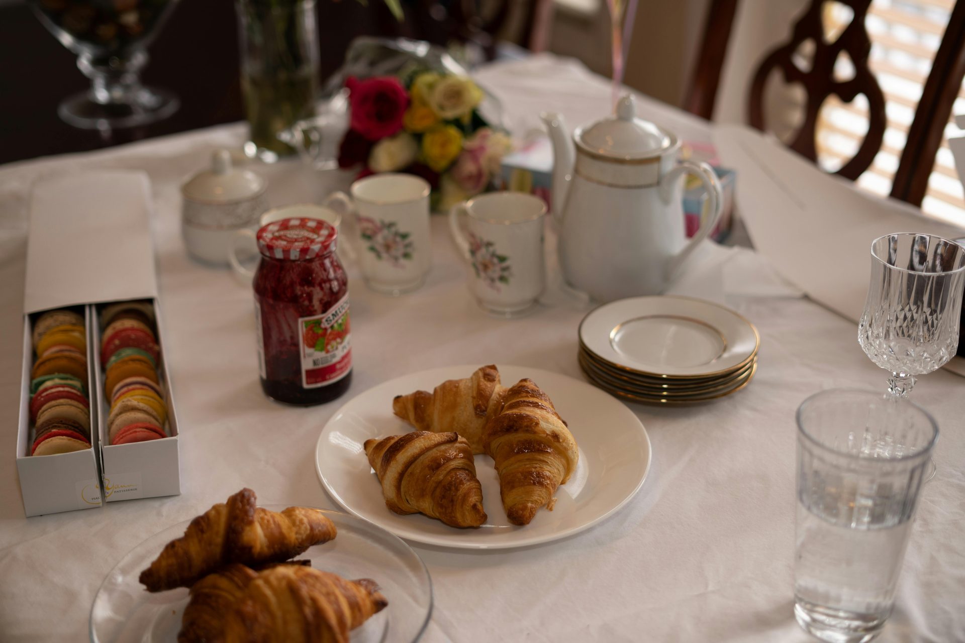 Une table de petit-déjeuner accueillante avec croissants, macarons et service à thé, pour un début de journée parfait.