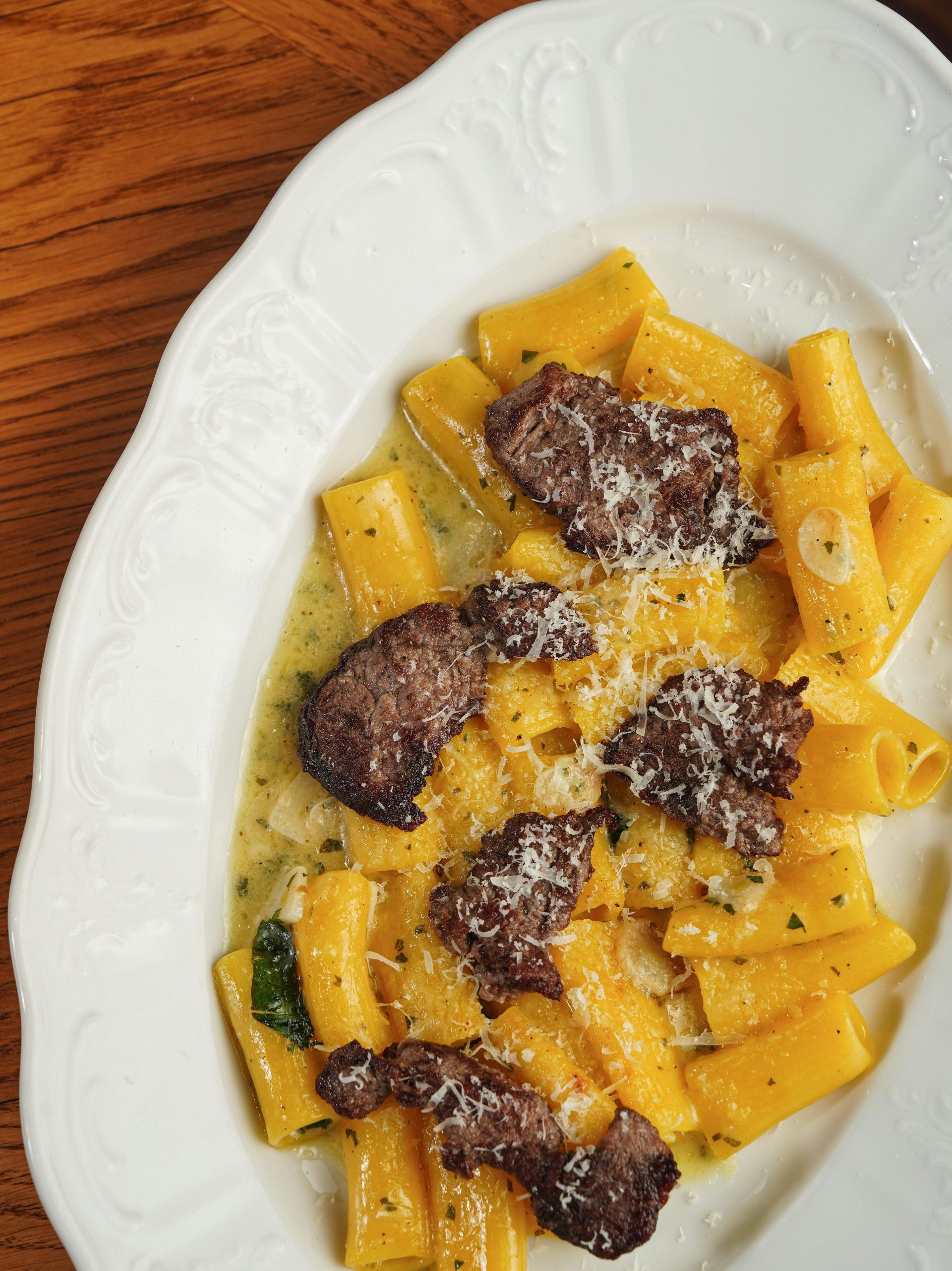 Pâtes rigatoni avec des tranches de bœuf savoureuses et du fromage, servies sur une assiette blanche.