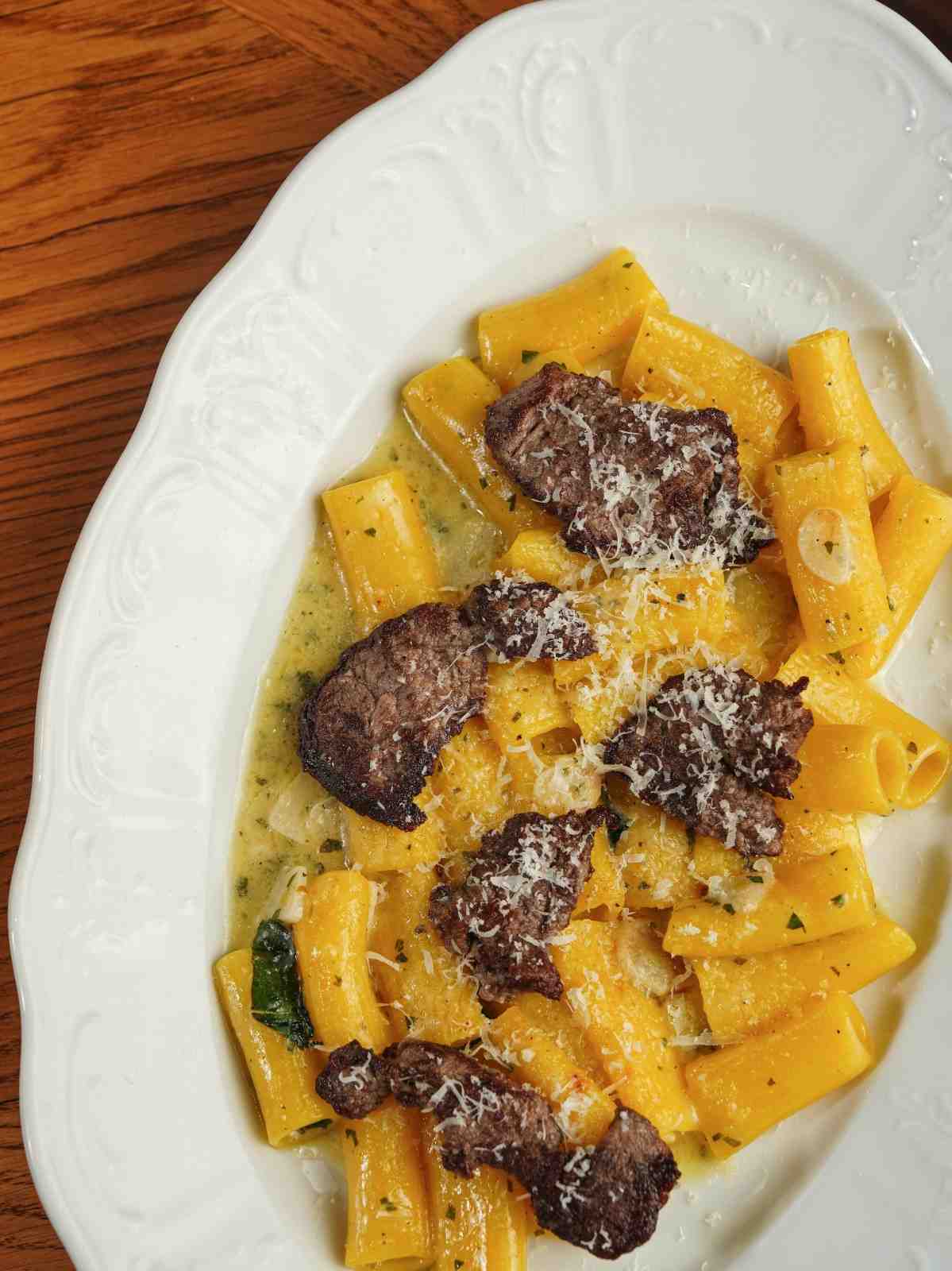 Pâtes rigatoni avec des tranches de bœuf savoureuses et du fromage, servies sur une assiette blanche.