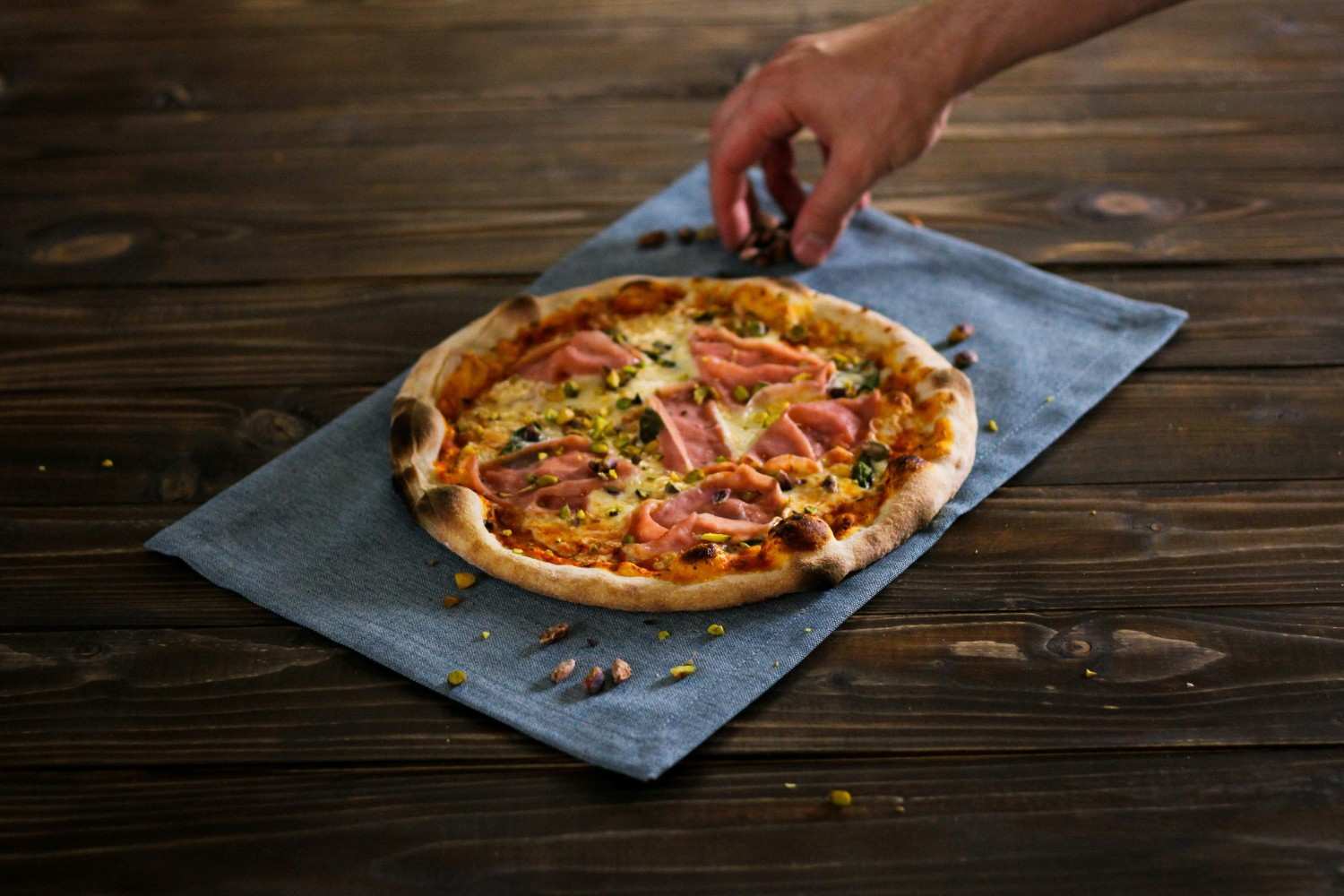 personne tenant une pizza sur une table en bois marron